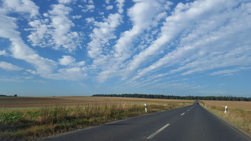 Empty road amidst fields against cloudy sky