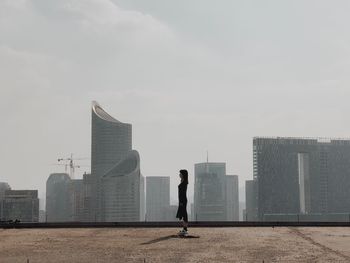 Side view of young woman standing on terrace against skyscrapers