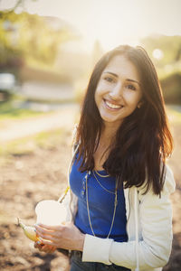 Portrait of happy female teenager holding disposable glass while standing outdoors