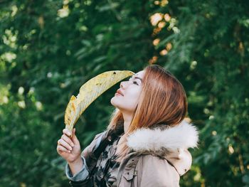 Woman holding leaf while standing against trees in park