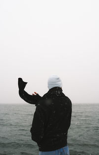 Rear view of man standing in sea against clear sky