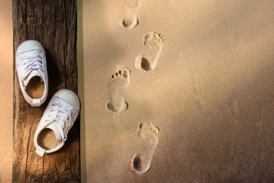 Directly above shot of shoes by footprints on sand at beach