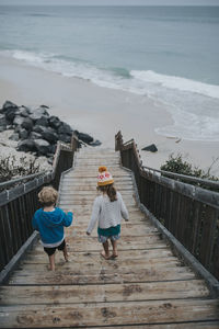 High angle view of siblings moving down steps leading towards beach