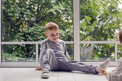 Two brothers sitting by the window in a white studio with green trees on the street