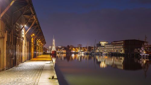 Illuminated buildings by river against sky at night