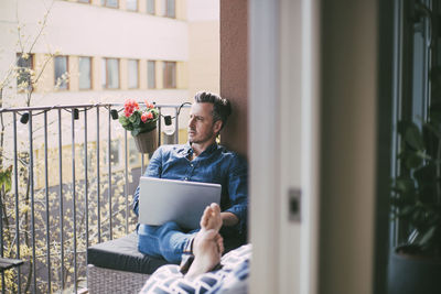 Man sitting on balcony with laptop looking out