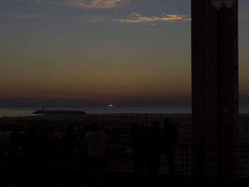 Silhouette people looking at sea against sky during sunset