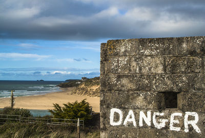 Danger sign on old wall at beach against sky