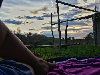 Low section of person relaxing on bed against sky