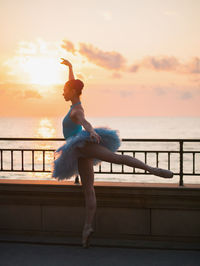 Woman ballet dancing by railing against sea