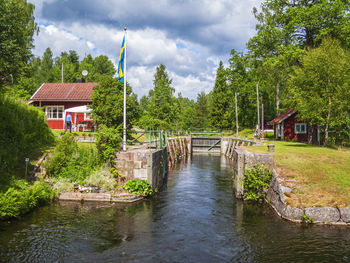Scenic view of river amidst trees and houses against sky