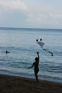 Silhouette child on shore at beach against sky