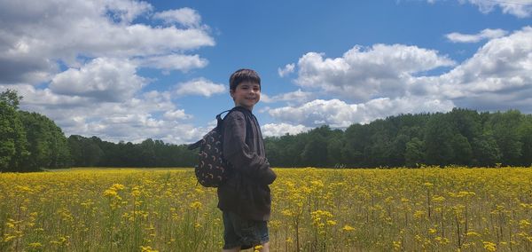 Portrait of man standing amidst yellow flowering plants on field against sky