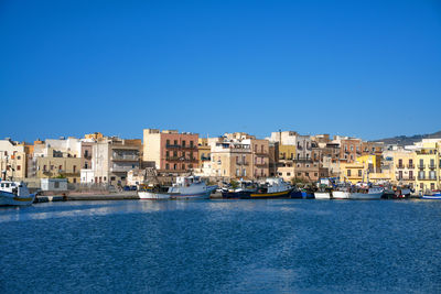 Buildings by sea against clear blue sky