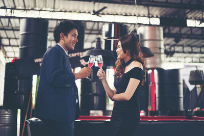 Side view of smiling couple toasting red wineglasses while standing in bar