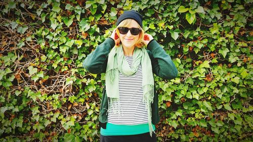 Young smiling woman standing against creeper plants