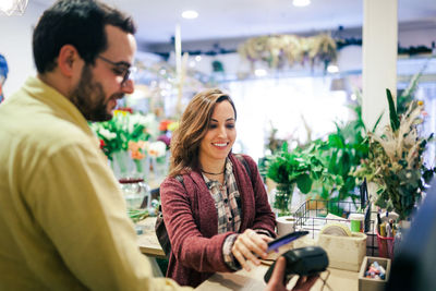 Smiling woman paying through credit card while standing with buyer at cash counter