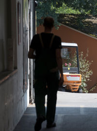 Rear view of man walking on sidewalk by building