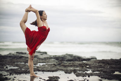 Woman dancing at beach against sky