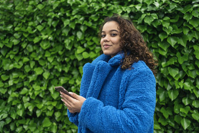 Young woman holding smart phone while standing outdoors