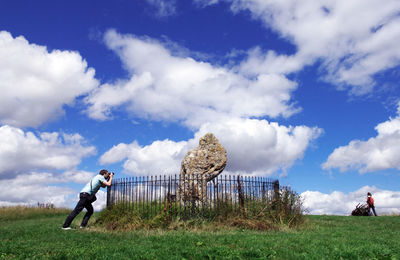 Side view of man photographing rock formation amidst fence at park