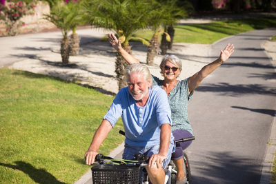 Smiling senior man with woman riding bicycle on road at park