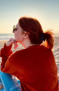 Rear view of young woman sitting at beach against sky