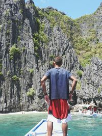 Rear view of man standing on rock against sky