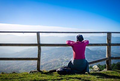 Rear view of woman sitting at observation point against sky