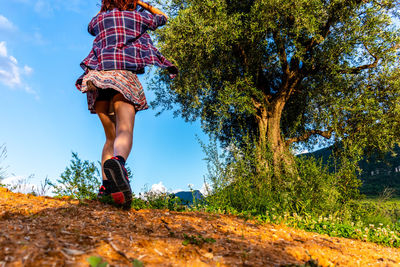 Low section of woman standing by tree against sky