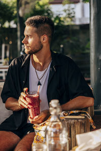 Man looking away holding smoothie glass while sitting at wellness resort