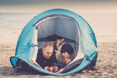 Couple with dog resting in tent at beach