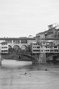 Arch bridge over river against buildings in city against clear sky