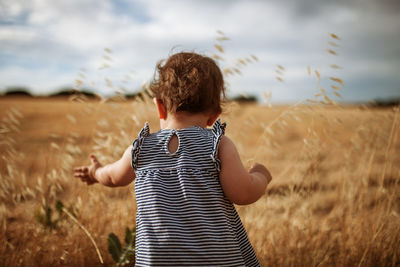 Rear view of cute baby standing on land against sky