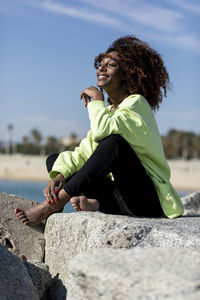 Smiling woman sitting on rock against sky