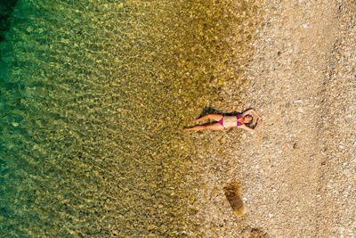 Aerial view of a girl having a sunbath on the pebble beach in the adriatic sea, croatia