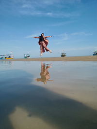Full length of woman jumping in sea against sky