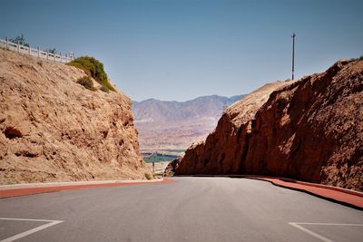 Road leading towards mountains against clear sky