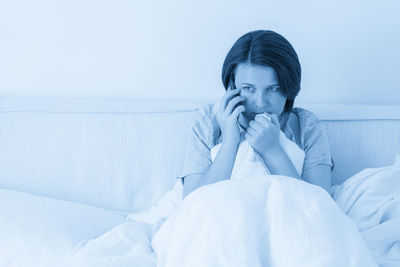 Young woman using mobile phone while lying on bed at home