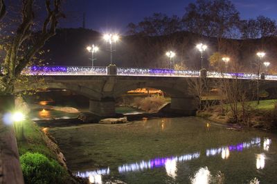 Illuminated bridge over river against sky at night