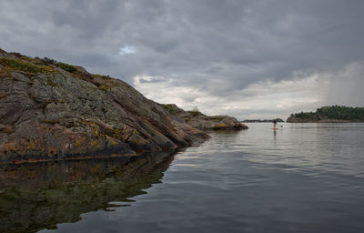 Man standing on rock by sea against sky