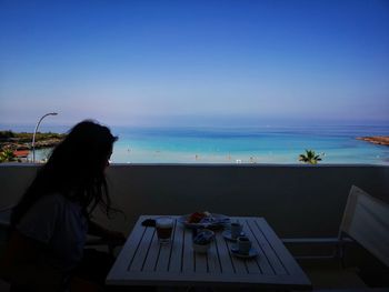 Woman relaxing on table by sea against clear blue sky