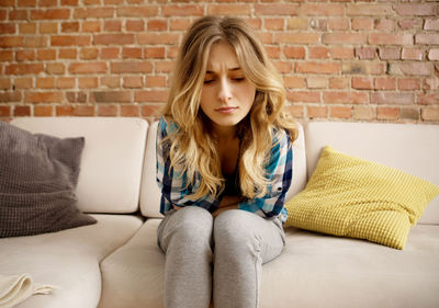 Portrait of teenage girl sitting on sofa against wall