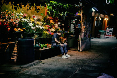People standing on sidewalk at night with flowers