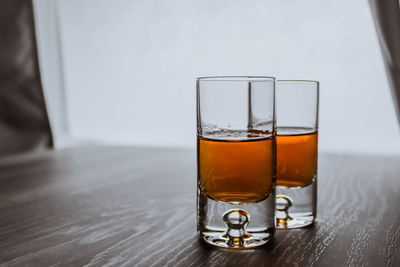 Two shot glasses with whiskey on a wooden background table next to window. space for text