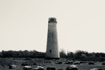 Lighthouse on field by building against clear sky