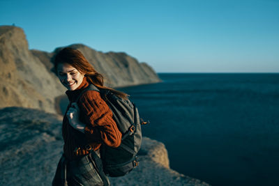 Young woman standing on rock by sea against sky