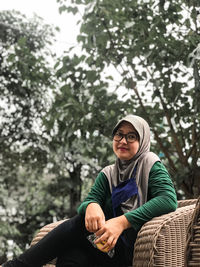 Portrait of young woman sitting on plant against trees