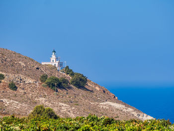 Lighthouse by sea against clear blue sky