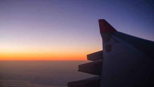 Silhouette airplane on sea against clear sky during sunset